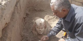 Arkeolog tørkar sand av sfinksstatuen.
